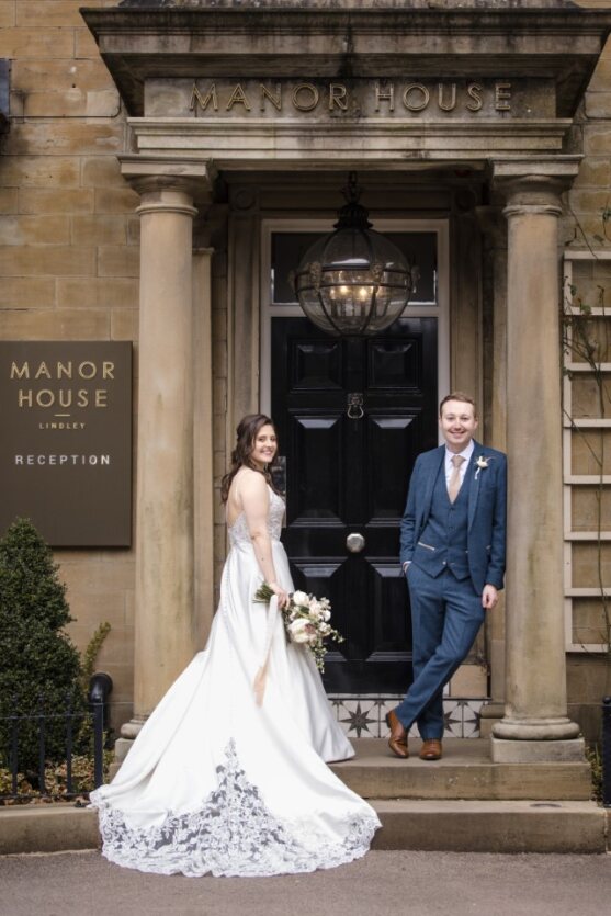 Wedding at Manor House Lindley. Bride and groom posing for a picture outside the entrance, with the bride holding flowers.