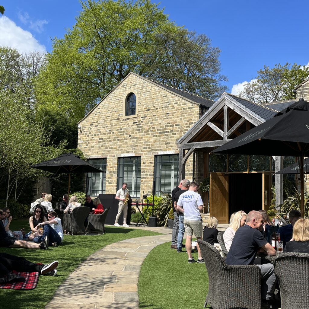 An outdoor picture in the sun at Manor House Lindley, with a band playing.