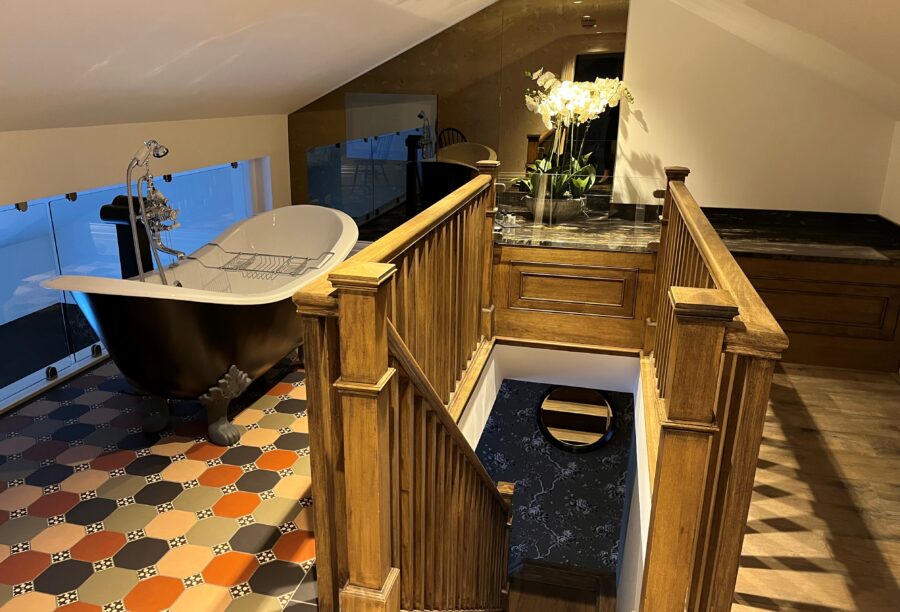 A view of the bathroom with a black roll-top bath and stairs leading down to the bedroom.