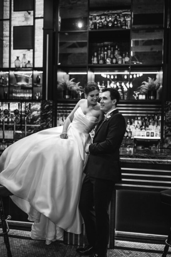Black and white picture of the bride and groom, with the bride sitting on the bar. Wedding at Manor House Lindley.