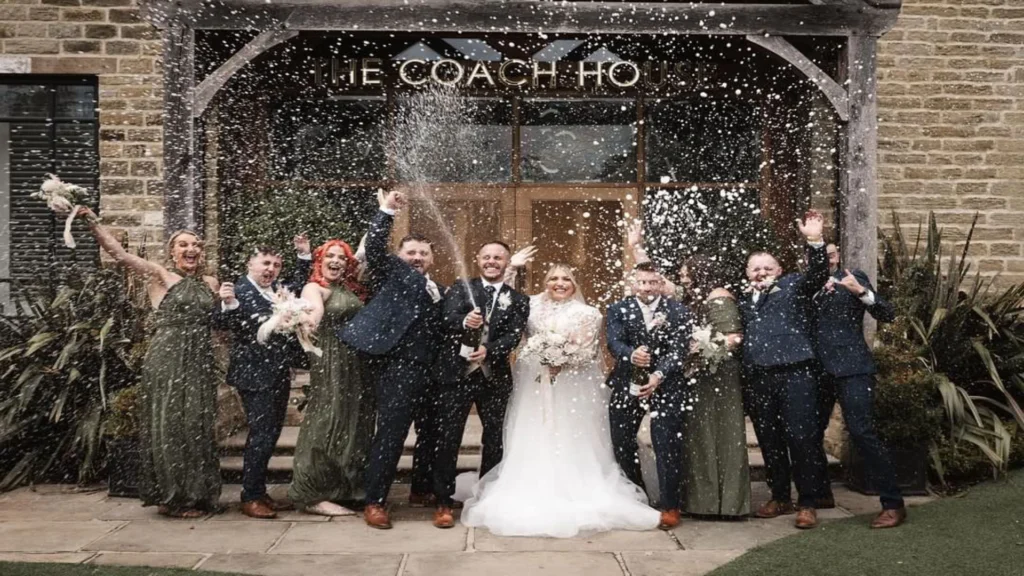 Bride and Groom with family and friends spraying champagne outside the wedding venue entrance at Manor House Lindley