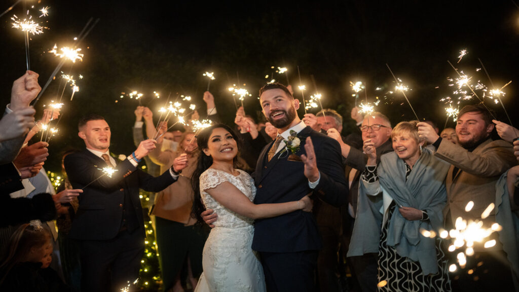 Bride and groom surrounded by family and friends holding sparklers at night