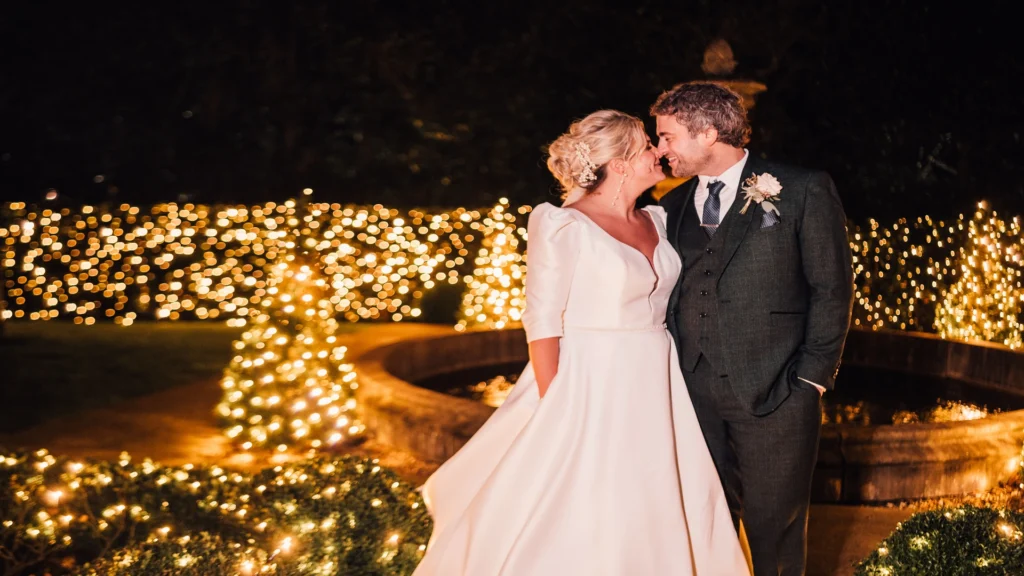 Bride and Groom kissing in the Manor House grounds with fairy lights behind them shining at night